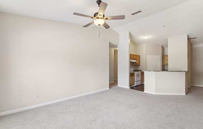 an empty living room with a ceiling fan and a kitchen