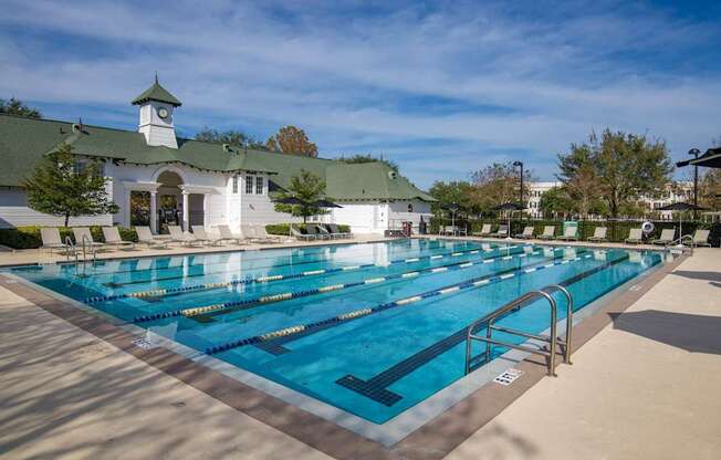 A large swimming pool in front of a white building with a green roof.