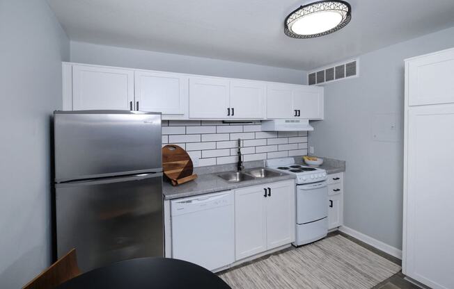 Fusion Fort Worth efficiency apartment in Haltom City kitchen with white dishwasher and stove, stainless steel refrigerator, and subway tile backsplash.