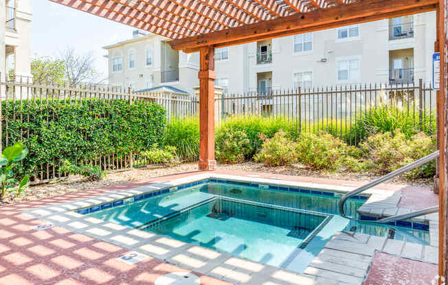 A small pool with a red tile border and a wooden pergola over it.