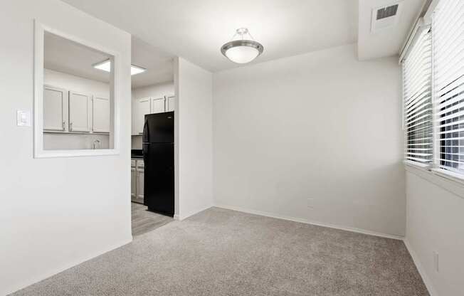 A room with a carpeted floor and a black refrigerator.