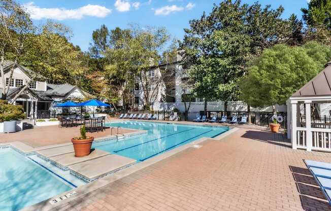 A large outdoor swimming pool surrounded by a brick patio and trees.
