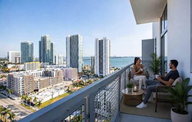 Two people sitting on a balcony overlooking a cityscape.