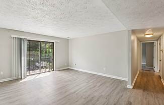A spacious room with wooden flooring and a sliding glass door leading to a patio.