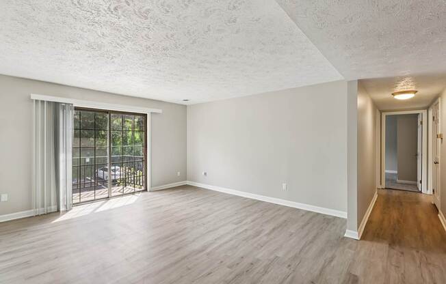 A spacious room with wooden flooring and a sliding glass door leading to a patio.