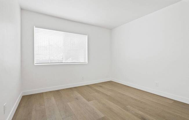 a bedroom with white walls and wood floors and a window