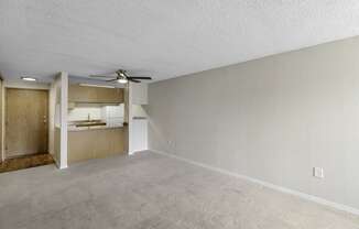 an unfurnished living room with a ceiling fan and a kitchen in the background at Willows Court Apartment Homes, Seattle, 98125