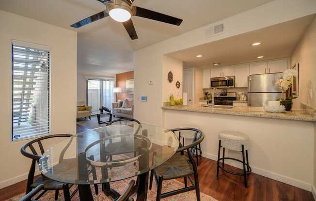 Model home dining area with ceiling fan. Open floor plan feel since you can view kitchen and living room from the dinning area. Dining table is set for four.