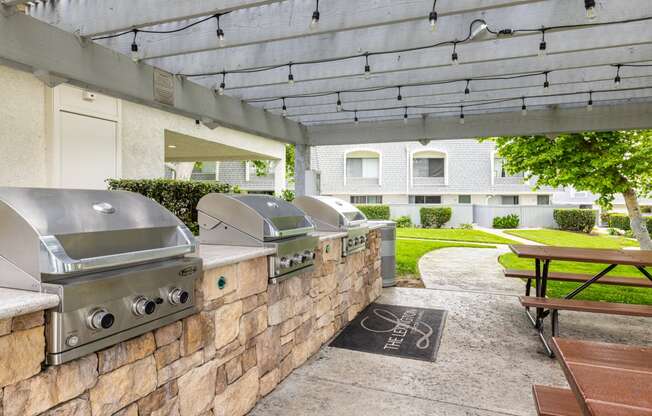 a covered patio with barbecue grills and a picnic table