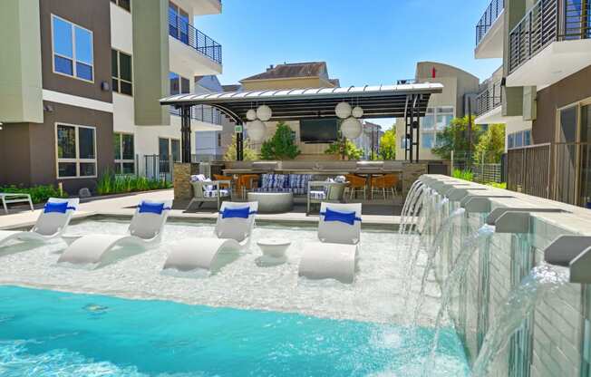 a pool with a waterfall and lounge chairs in front of a building