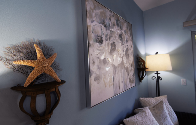 A starfish sits on a table next to a painting and a lamp.