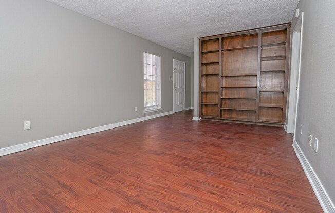 Unfurnished apartment living room with wooden floors and wooden built-in shelving at Magnolia apartments in Shreveport, LA