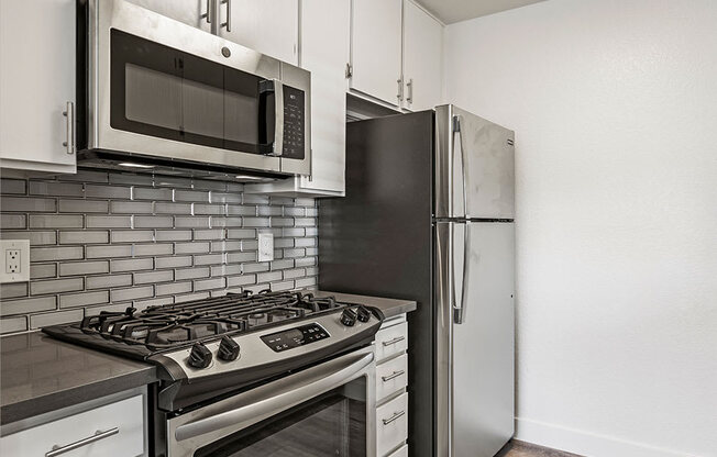 White tiled kitchen with stainless steel fridge, oven, and microwave.