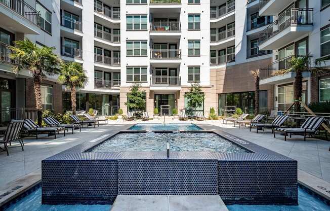 A large pool in the middle of a courtyard surrounded by lounge chairs and palm trees.