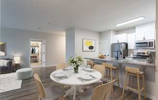 a dining area with a white table and chairs and a kitchen in the background