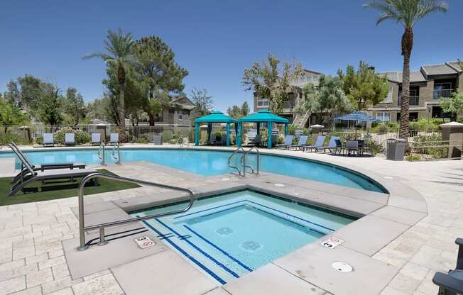 A swimming pool and spa with large trees and blue umbrellas.