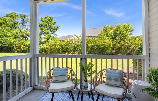 Two chairs are on a porch with a view of a house and trees.