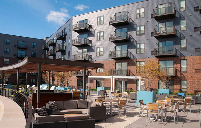 Outdoor community kitchen and lounge area, with tables and couches, balconies in background