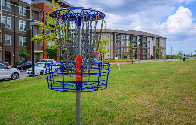a frisbee hoop in the grass in front of an apartment building