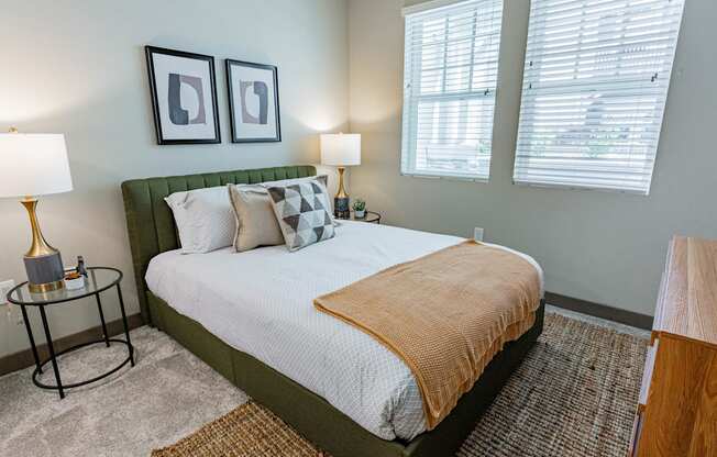 Bayswater Burlingame - Spacious Bedroom With Plush Carpet Flooring, Area Rug, Bed, Nightstands With Lamps, Dresser, Wall Art, And Two Windows With Blinds at Bayswater Apartments, Burlingame, CA