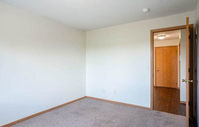 A room with a carpeted floor and a wooden door. Bismarck, ND Sierra Ridge Apartments