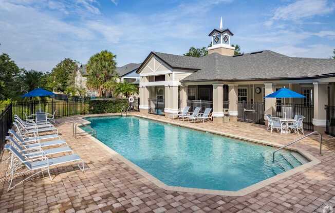 A pool surrounded by chairs and umbrellas in front of a house.