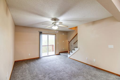 an empty living room with a ceiling fan and a door to a balcony