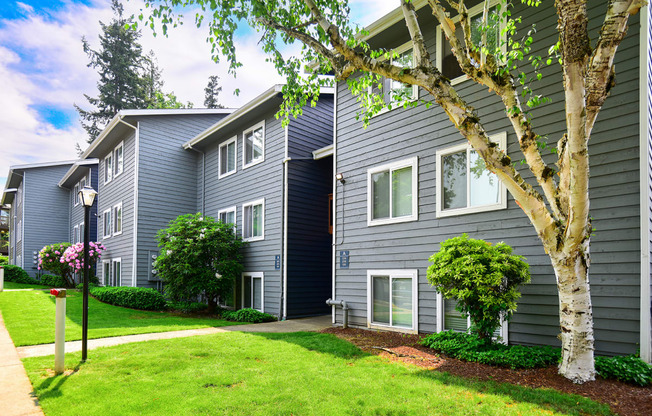 a gray building with white trim and a tree in front of it