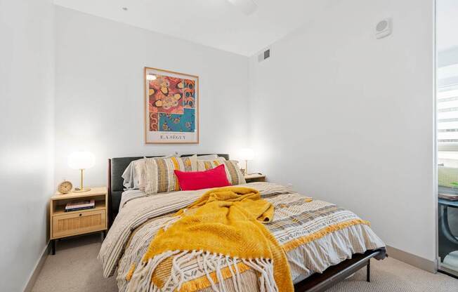 A bedroom with a bed, a nightstand with a lamp, and a framed picture on the wall.