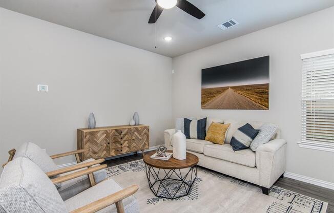 3-BR Homes for Rent in Katy, TX - Villas at Sunterra - Living Room with a Couch, Two Chairs, a Coffee Table, a Ceiling Fan, Wood-Style Flooring, a Window, and Stylish Decor