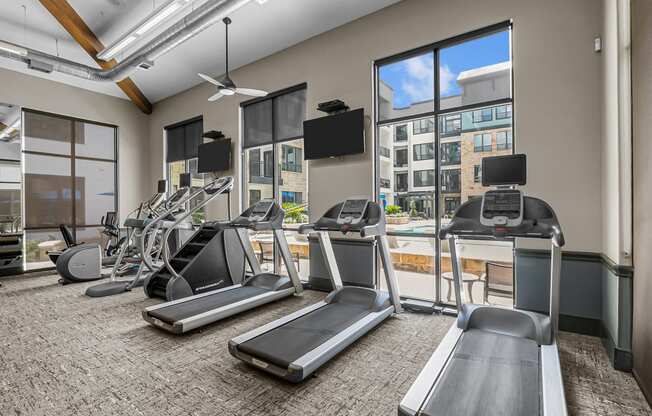 a gym with cardio equipment and windows with a view of the city