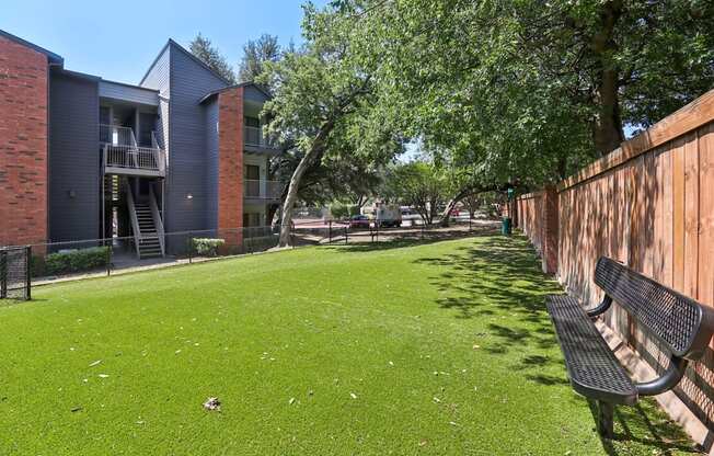 A grassy area with a bench and apartment buildings in the background.