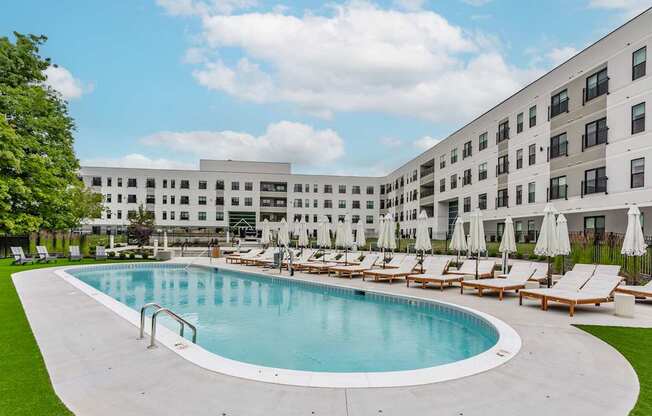 A large swimming pool surrounded by sun loungers and umbrellas in front of a modern building.