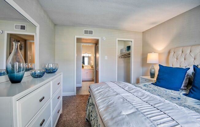 A bedroom with a large bed and a dresser with vases on top.