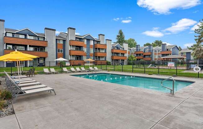 A pool area with a yellow umbrella and lounge chairs in front of a multi-story apartment building. at Northpoint Apartments, Tacoma, WA, 98407