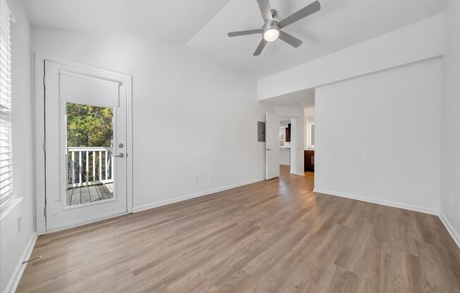 an empty living room with a ceiling fan and a door to a balcony