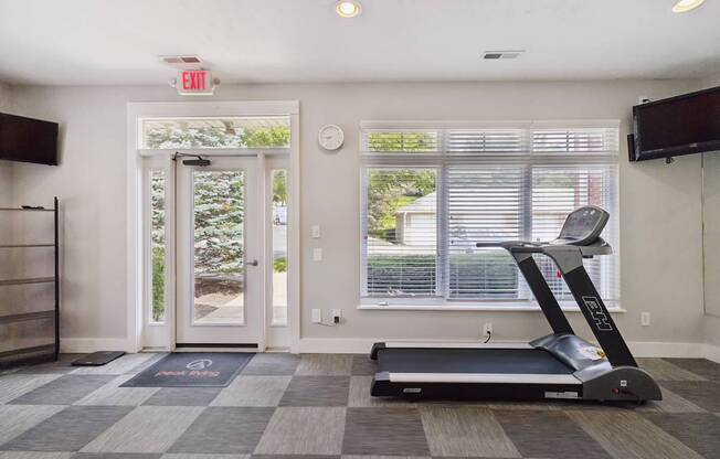 A treadmill is in a room with a window and a clock on the wall.