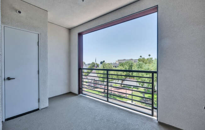 A room with a large window overlooking a balcony with a view of a building and trees.