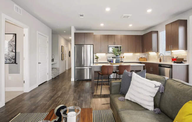A modern kitchen and living room with a grey couch and wooden floors.