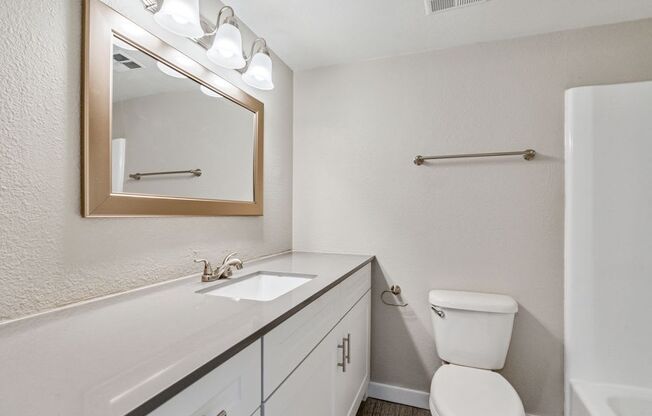 A bathroom with a white toilet, sink, and mirror.