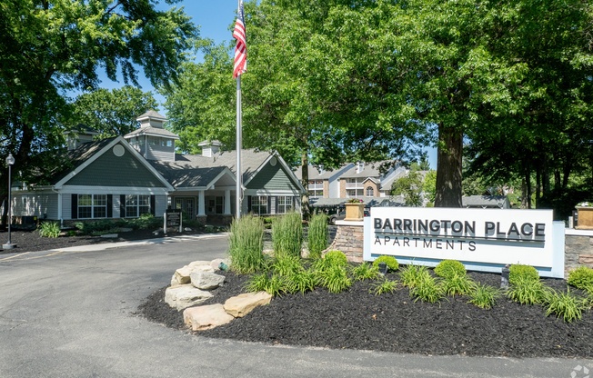 the entrance to barrington place apartments with a sign and an flag