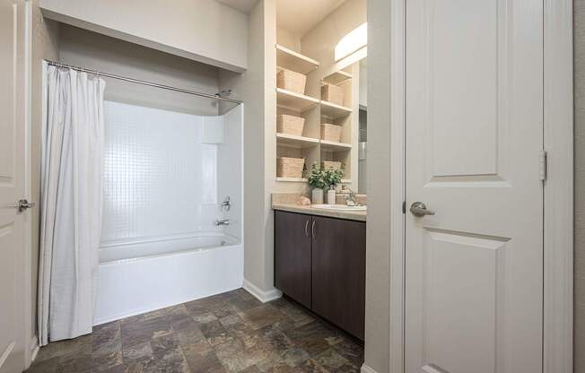 A bathroom with a tub, sink, and a cabinet with shelves.