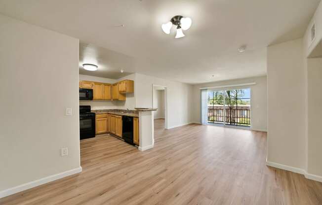 an empty living room and kitchen with wood flooring and a large window