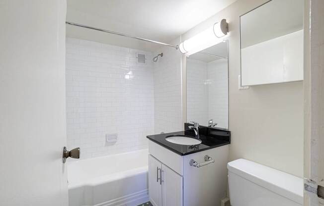 A white bathroom with a black counter top and a white tub.