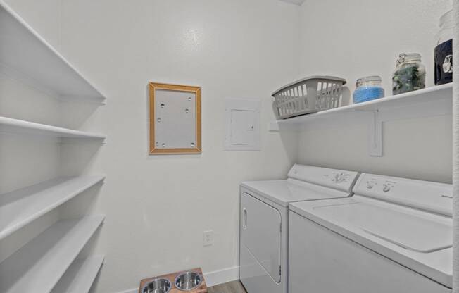 a white laundry room with a washer and dryer and shelves