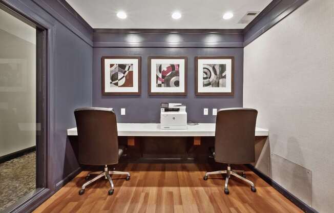 Two brown chairs are placed in front of a desk with a laptop and a printer on it.