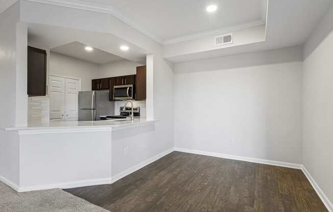 an empty living room with a kitchen and a hard wood floor