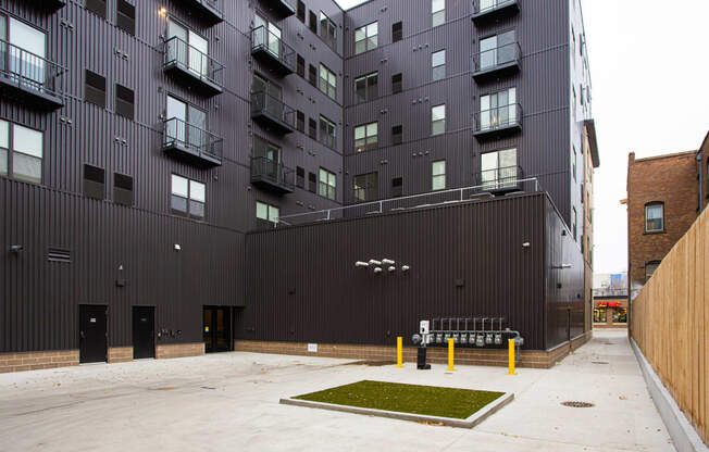 A courtyard with a bench and grass patch in front of a black building  at Mercantile on Broadway, Fargo, North Dakota 58102