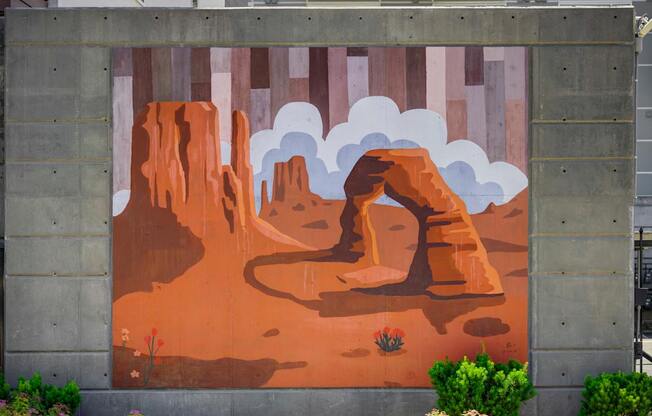 A mural of a desert scene with a large rock formation and a small plant in the foreground.