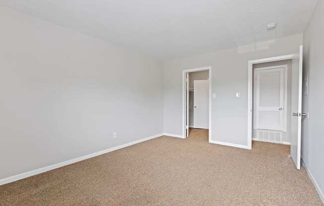 a bedroom with white walls and carpet and a door to a closet